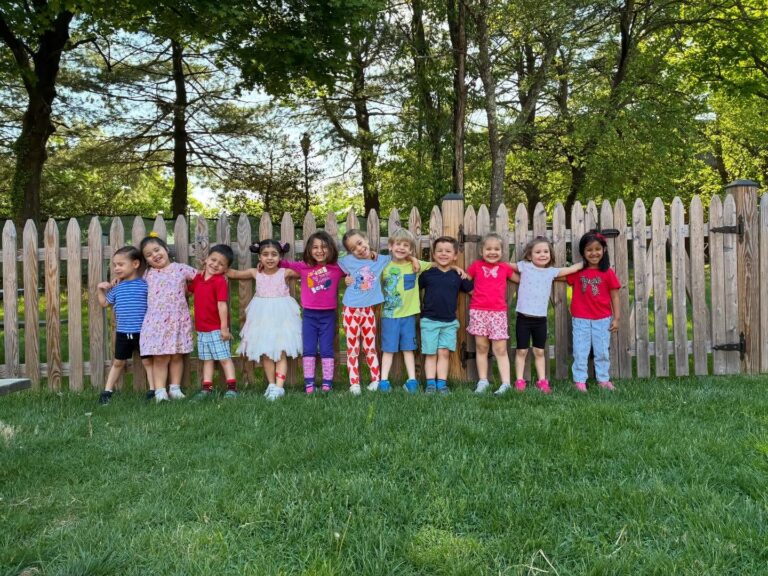 Preschool students lined up and smiling at the playground fence