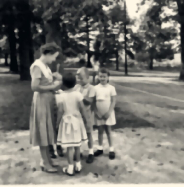 A teacher talks with three young students on the school grounds, 1961